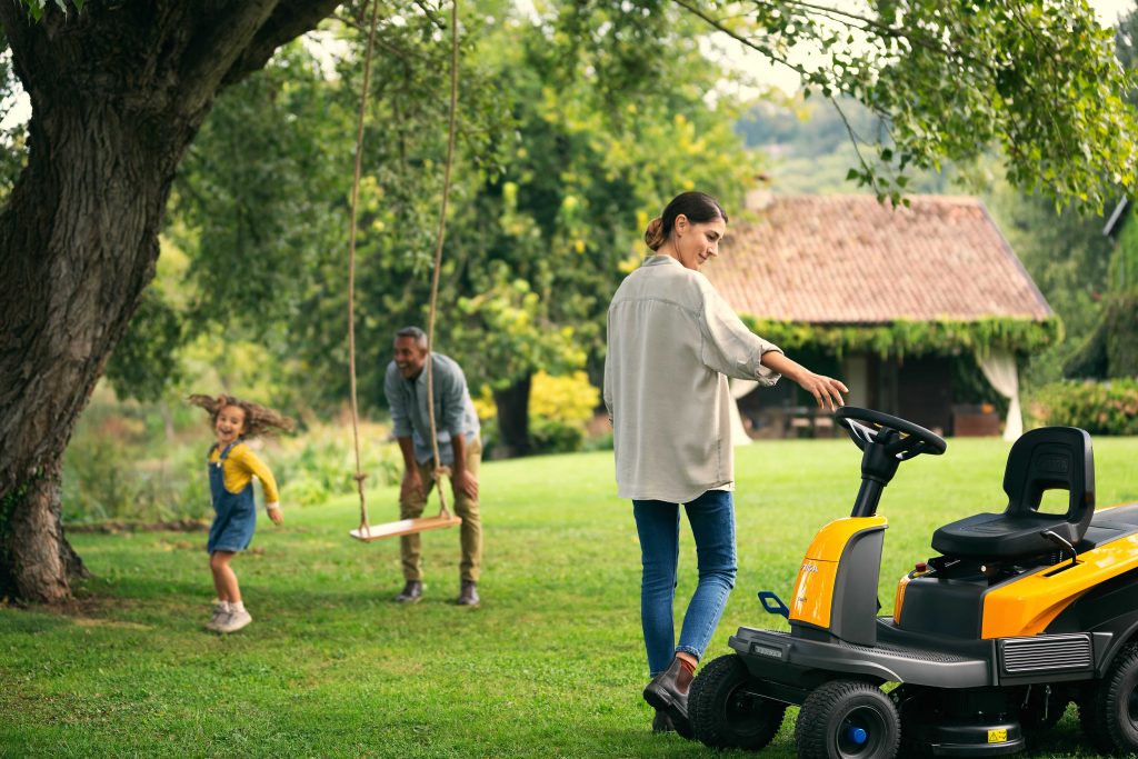 Man on yellow riding lawn mower with family nearby