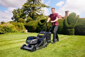 Man operating self-propelled lawn mower on grass.