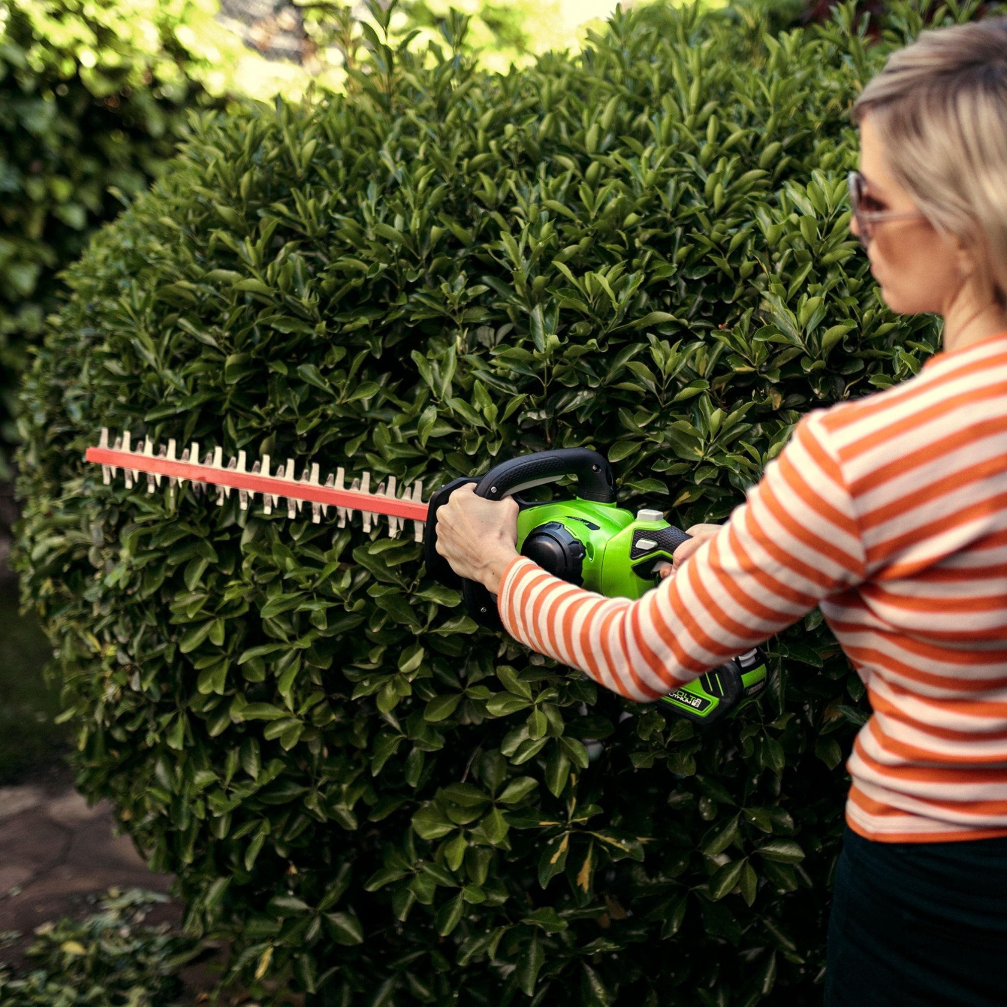2shig0ffbbj.jpg - Mowers Online Woman using electric hedge trimmer on shrub