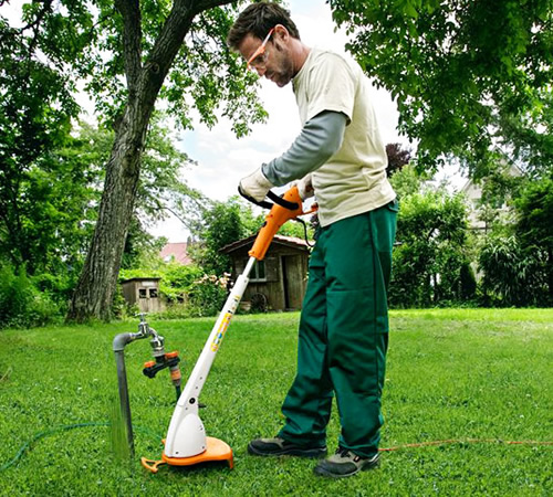 bjtswdd0x0l.jpg - Mowers Online Man using string trimmer on grass lawn