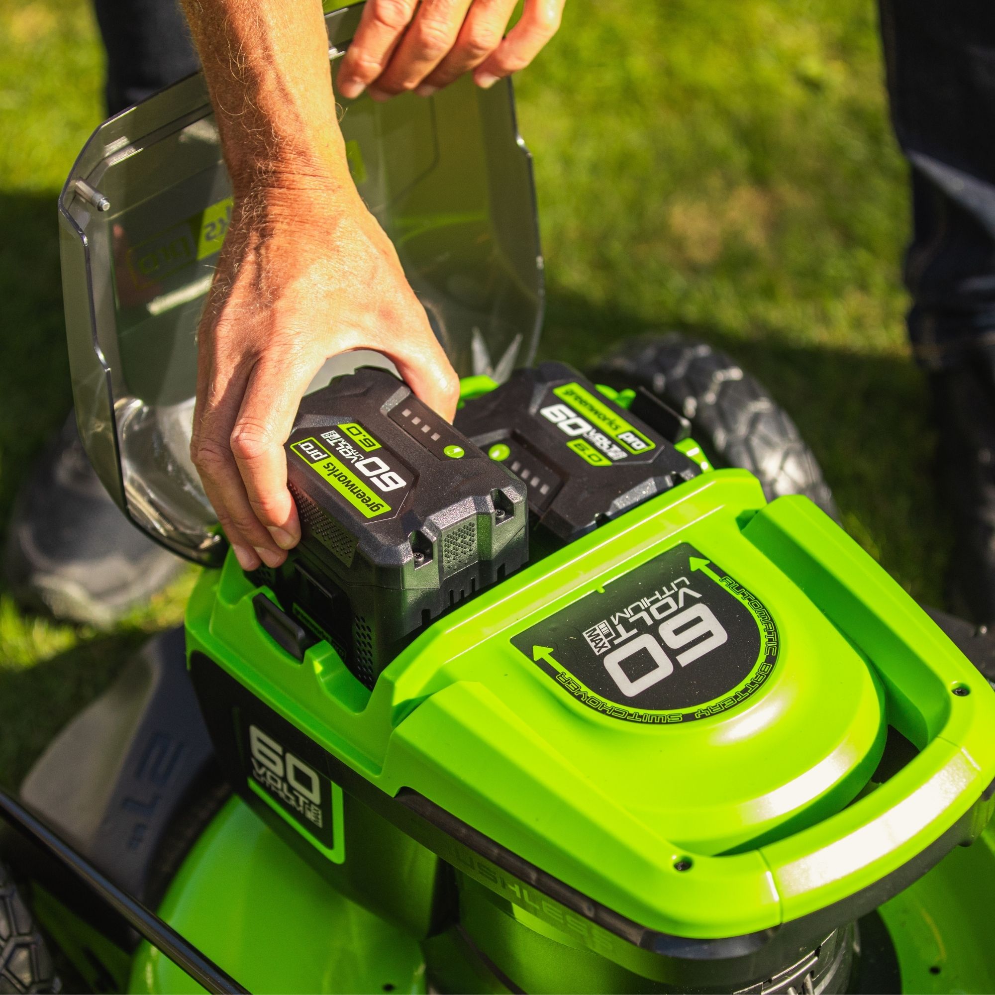 finmsbe5wei.jpg - Mowers Online Person holding green lawn mower with batteries