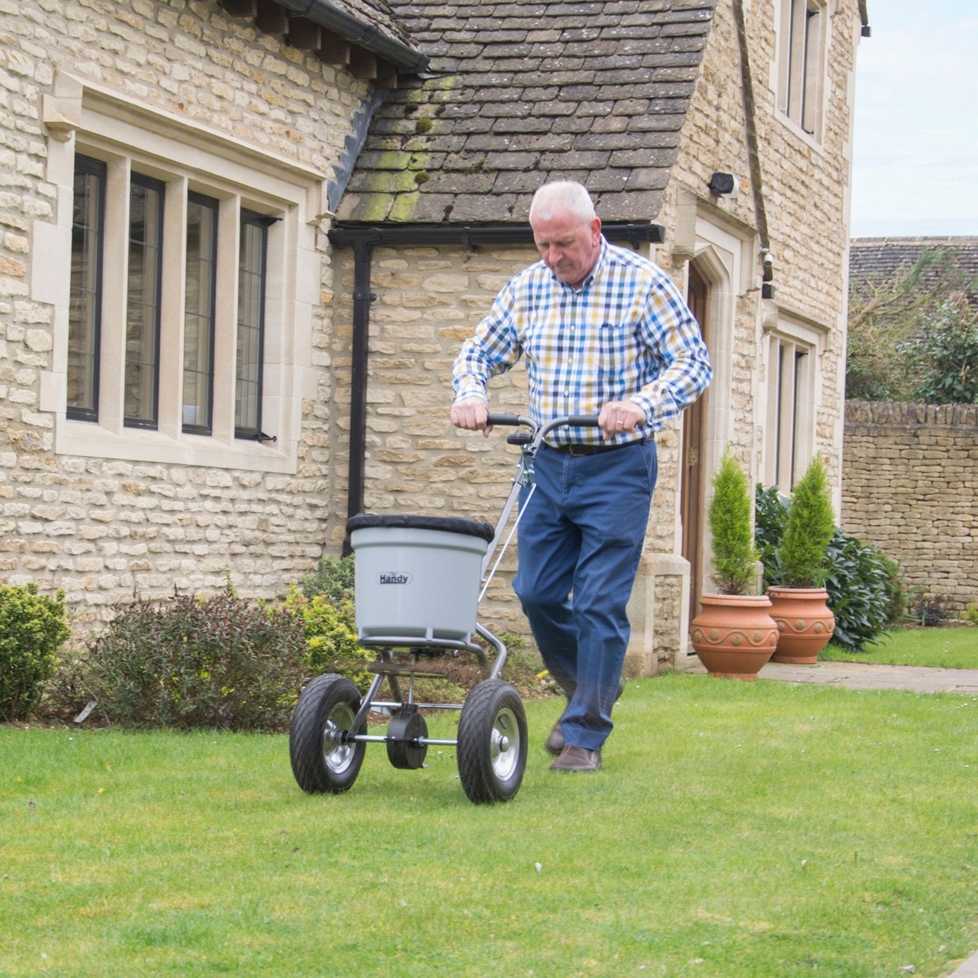 kntyv5ylhra.jpg - Mowers Online Man using wheeled garden spreader on lawn